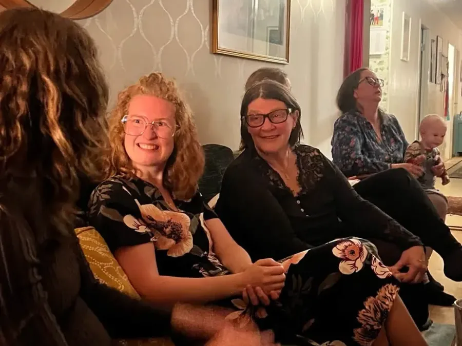 Kvinnor sitter i en soffa och samtalar under en filmkväll hemma i varmt lampljus.