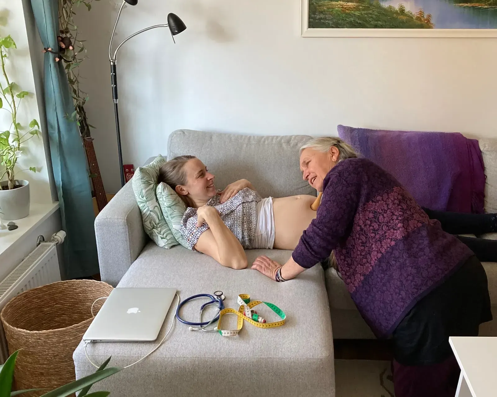 Hembarnmorskan lyssnar på fosterljuden med tratt på den gravida magen under ett hembesök i vardagsrummet.