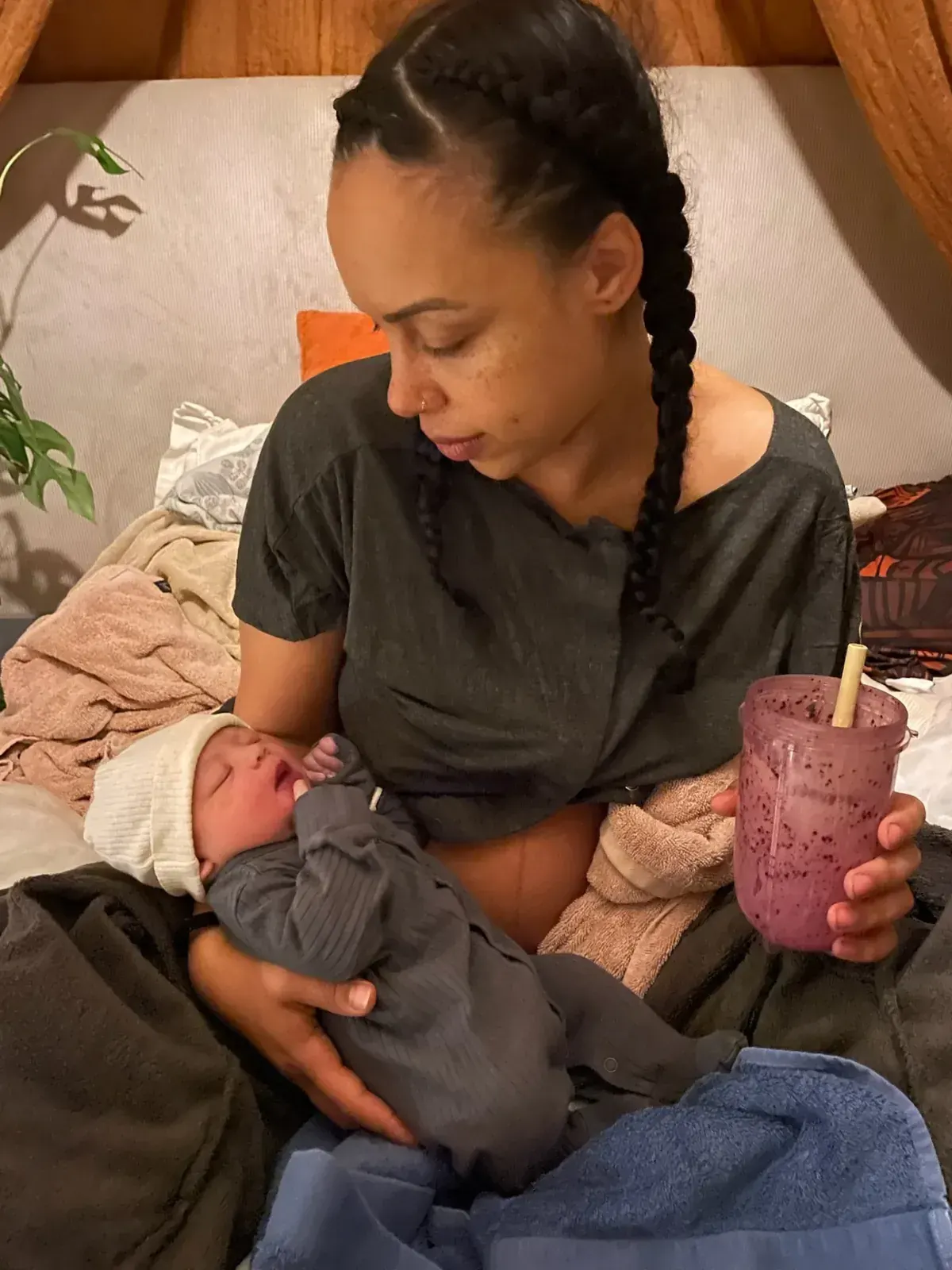 Isa sitter på sängen med sin nyfödda dotter i famnen direkt efter hemfödseln.