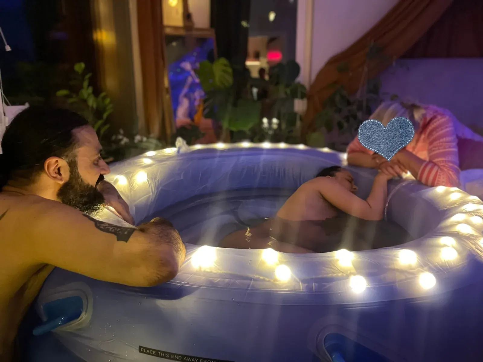 Isas partner vid kanten av den upplysta förlossningspoolen medan Isa vilar i vattnet.