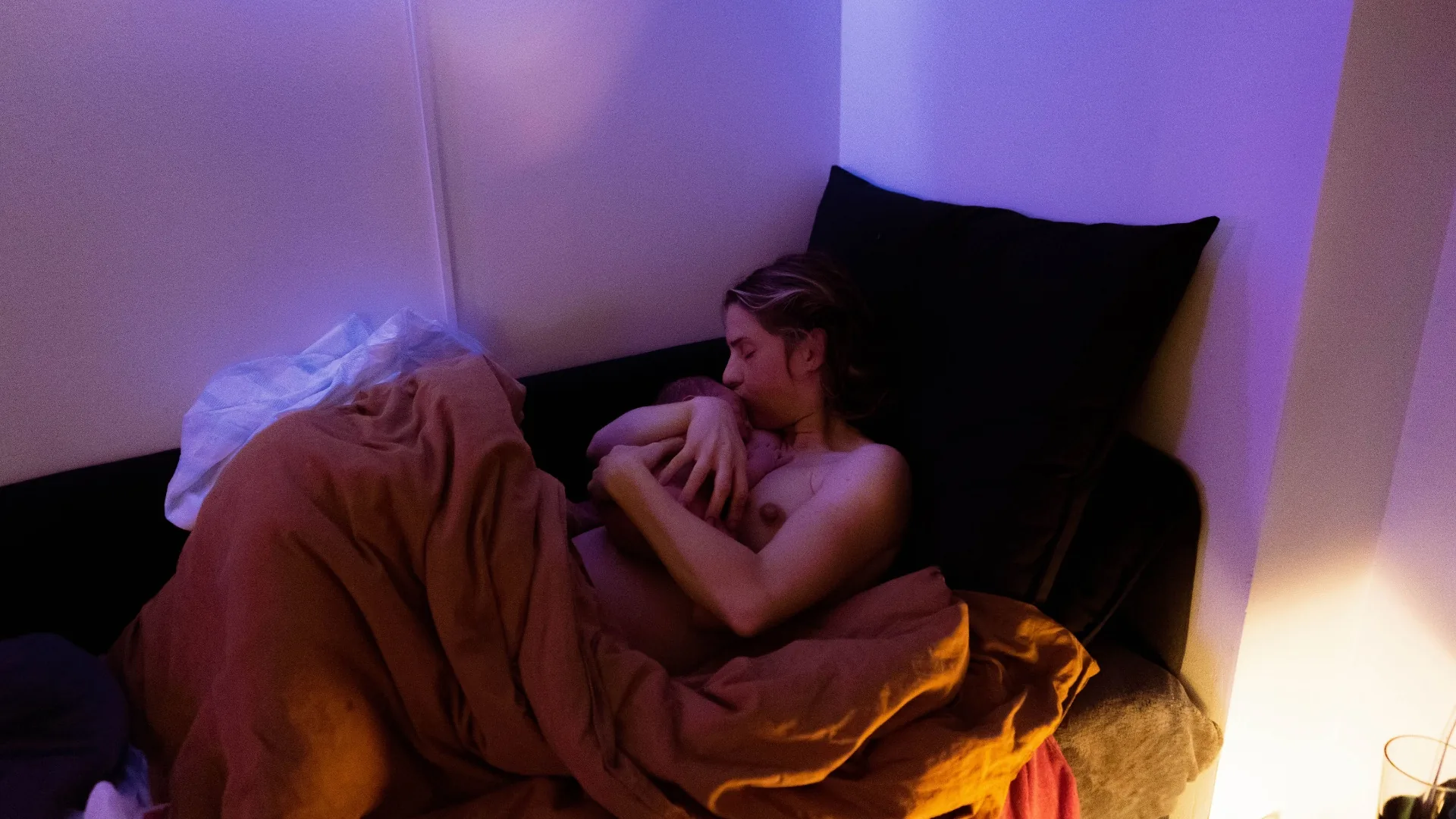 Jessica vilar mot kuddarna med nyfödde Rio i famnen, insvept i en rostfärgad filt.