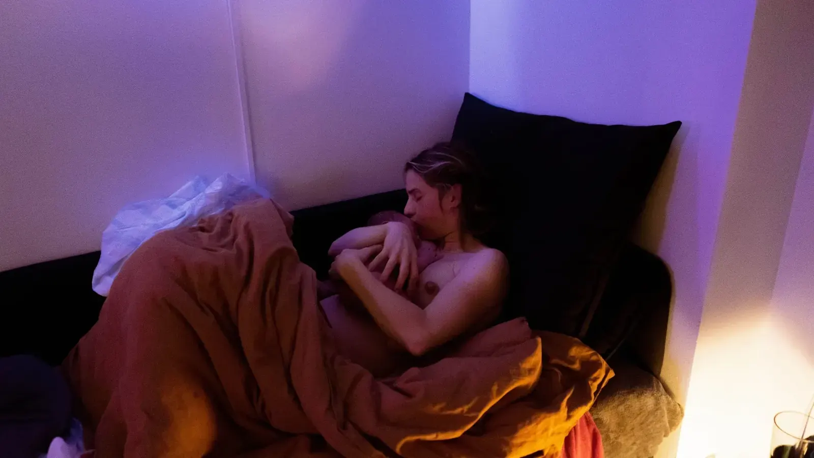 Jessica vilar mot kuddarna med nyfödde Rio i famnen, insvept i en rostfärgad filt.