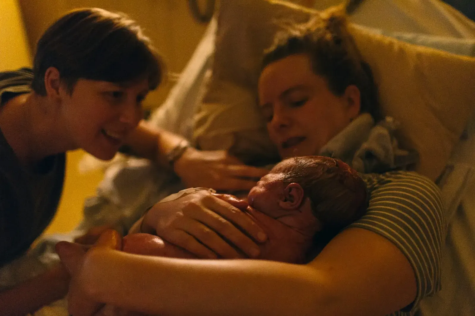 Linda och hennes fru ser kärleksfullt på sin nyfödda dotter som vilar hud mot hud på bröstet.