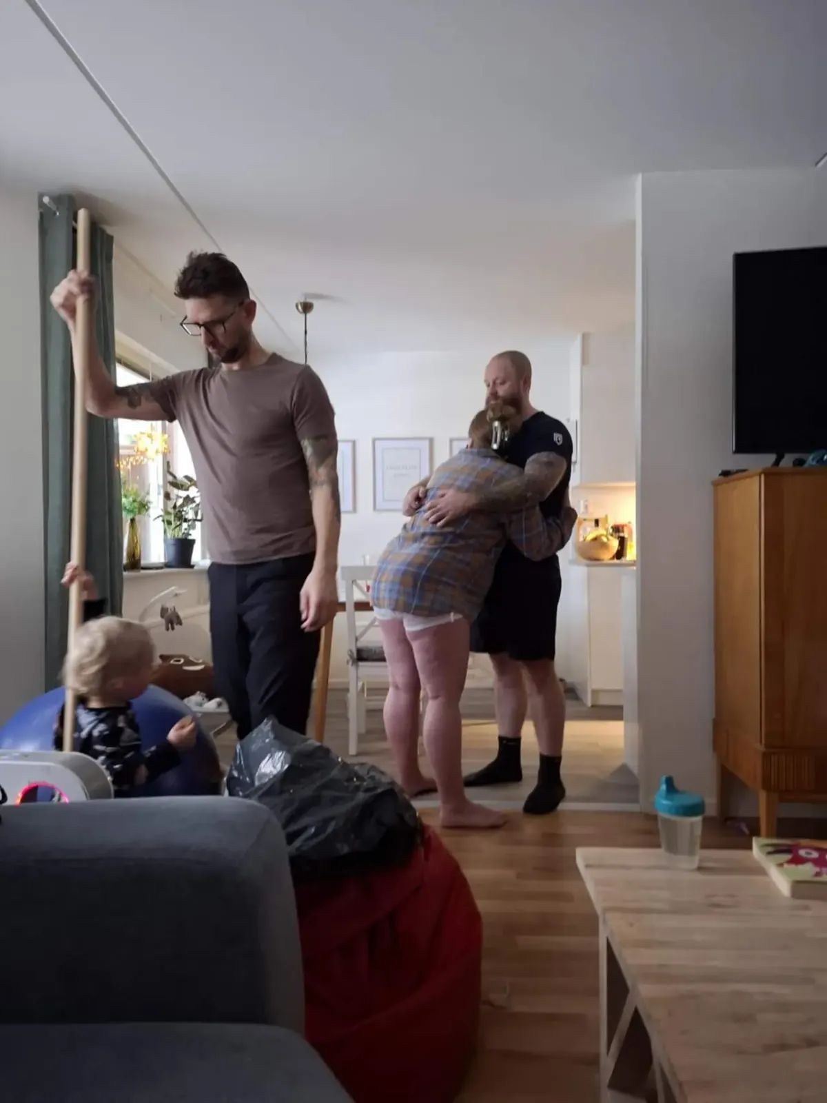 Lisette står lutad mot sambon i vardagsrummet, doulan håller en stödpinne och äldsta sonen leker bredvid.