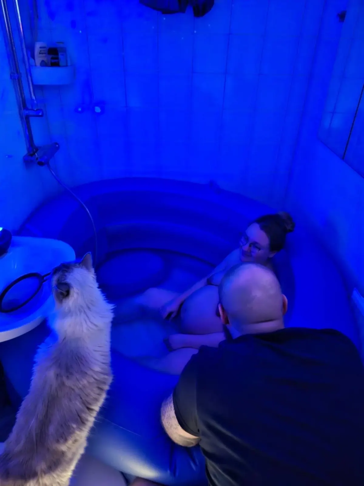 Lisette vilar i förlossningspoolen i blått ljus medan sambon sitter intill och katten kommer fram för att hälsa.