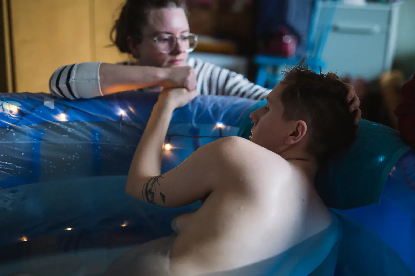 Matilda vilar i förlossningspoolen hemma medan en stödperson håller hennes hand över poolkanten.