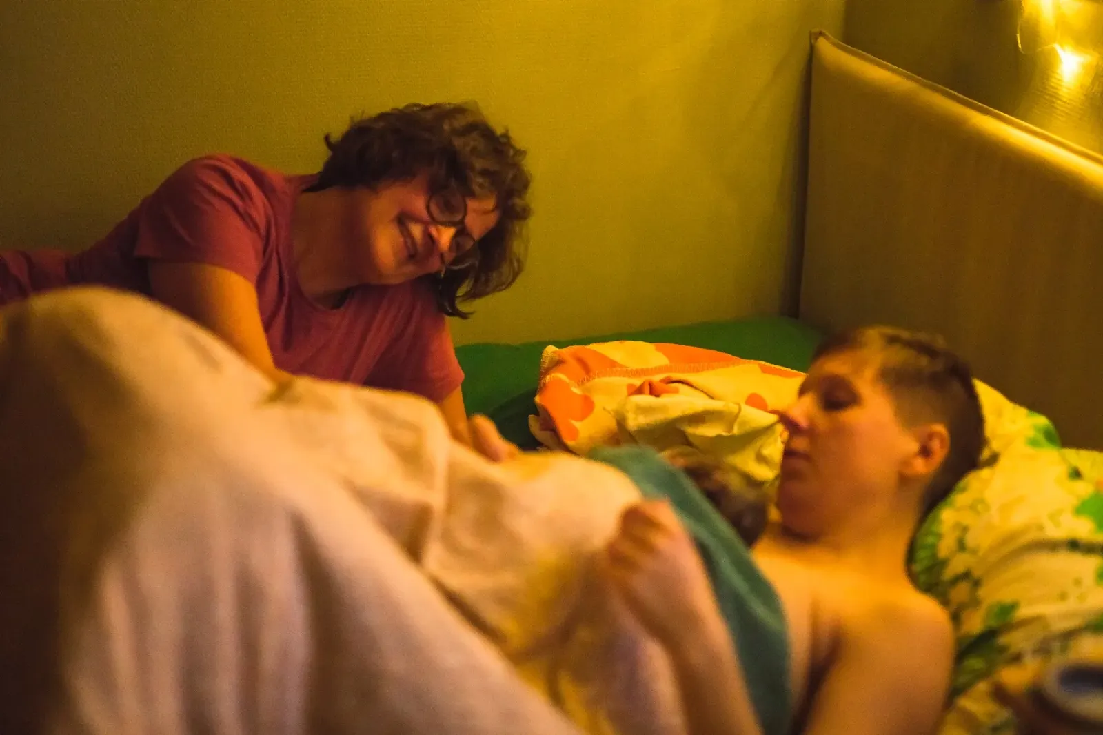 Matildas mamma lutar sig leende mot Matilda som vilar i sängen med sitt nyfödda barn hud mot hud efter hemfödseln.