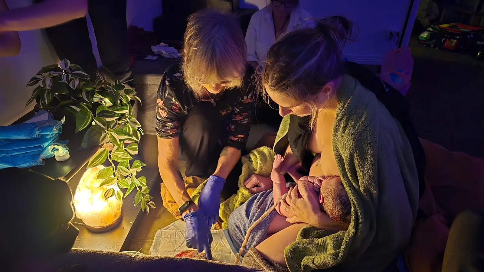 Barnmorska och mamma med nyfödd bebis i hemmet, varmt ljus från saltsten.