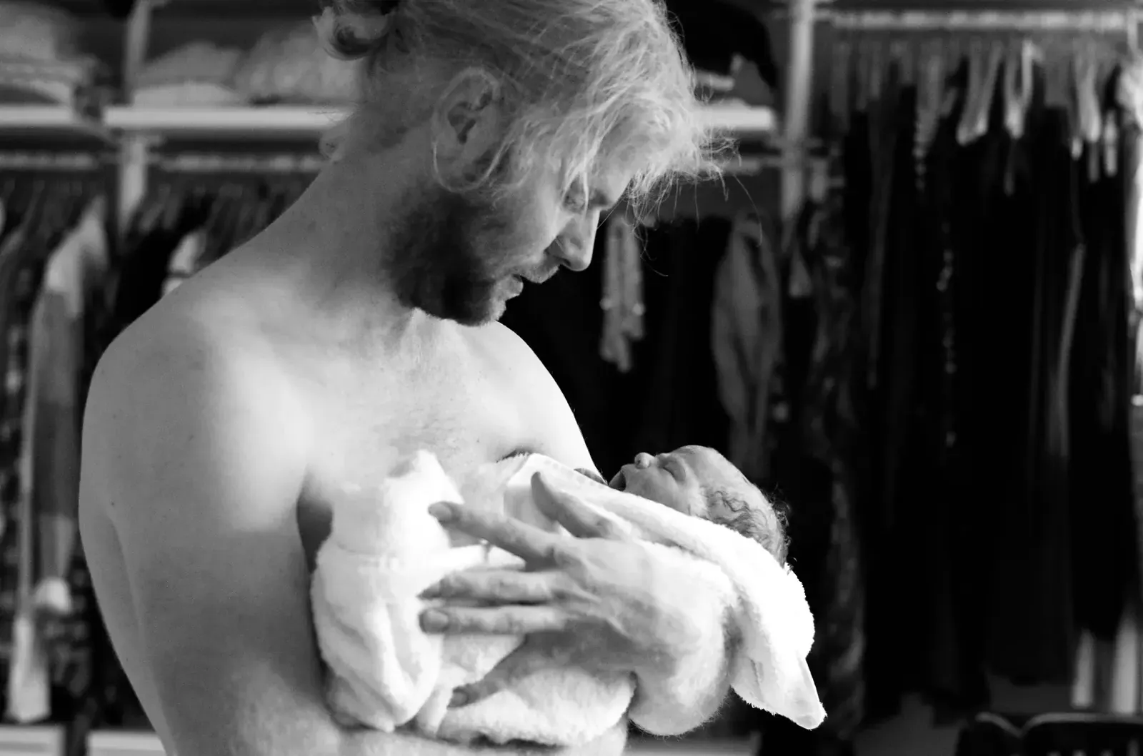 Nybliven pappa håller sin nyfödda bebis insvept i en handduk mot bröstet kort efter hemfödseln.