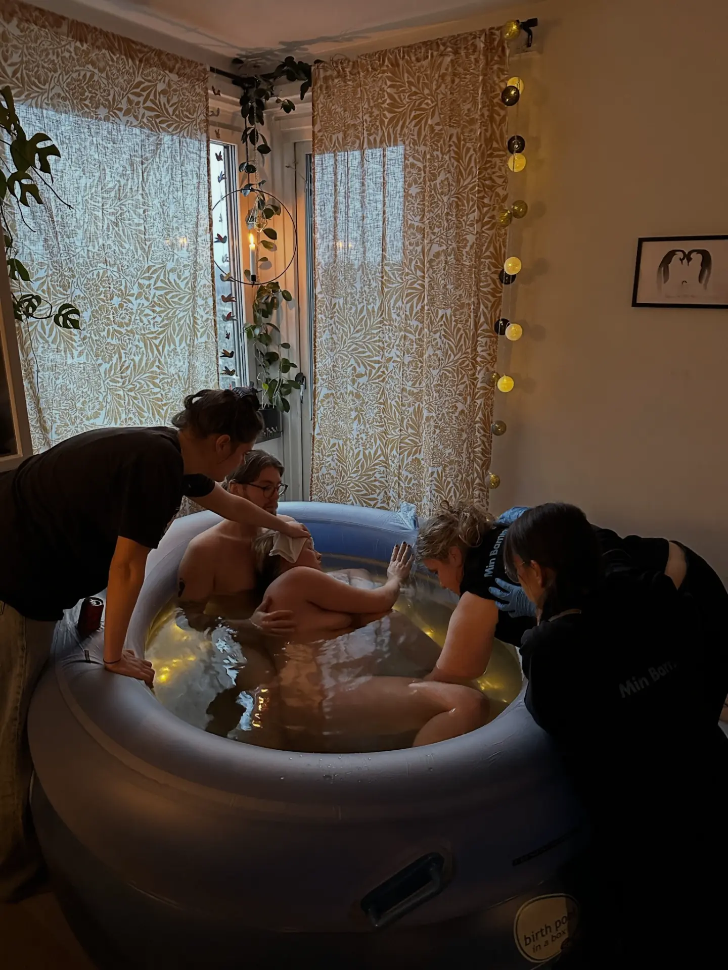 Sigrid och hennes man i förlossningspoolen medan barnmorskorna stöttar runtomkring och rummet är upplyst av varm ljusslinga.