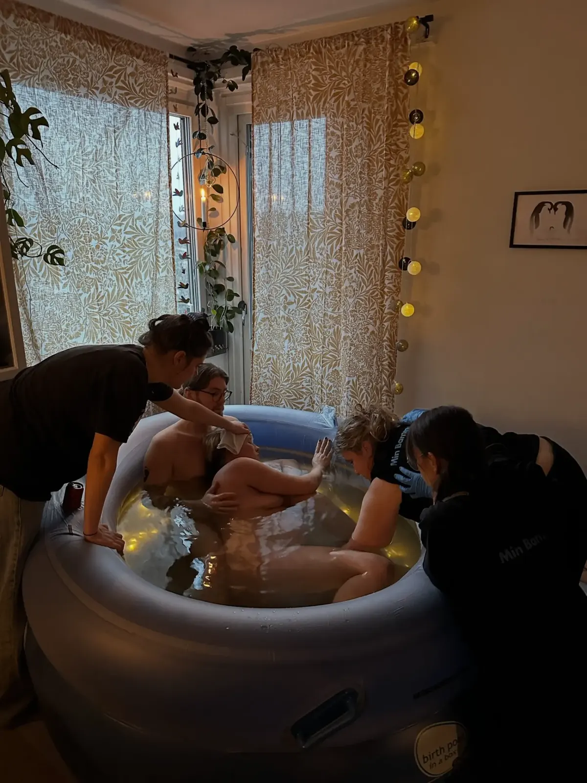 Sigrid och hennes man i förlossningspoolen medan barnmorskorna stöttar runtomkring och rummet är upplyst av varm ljusslinga.